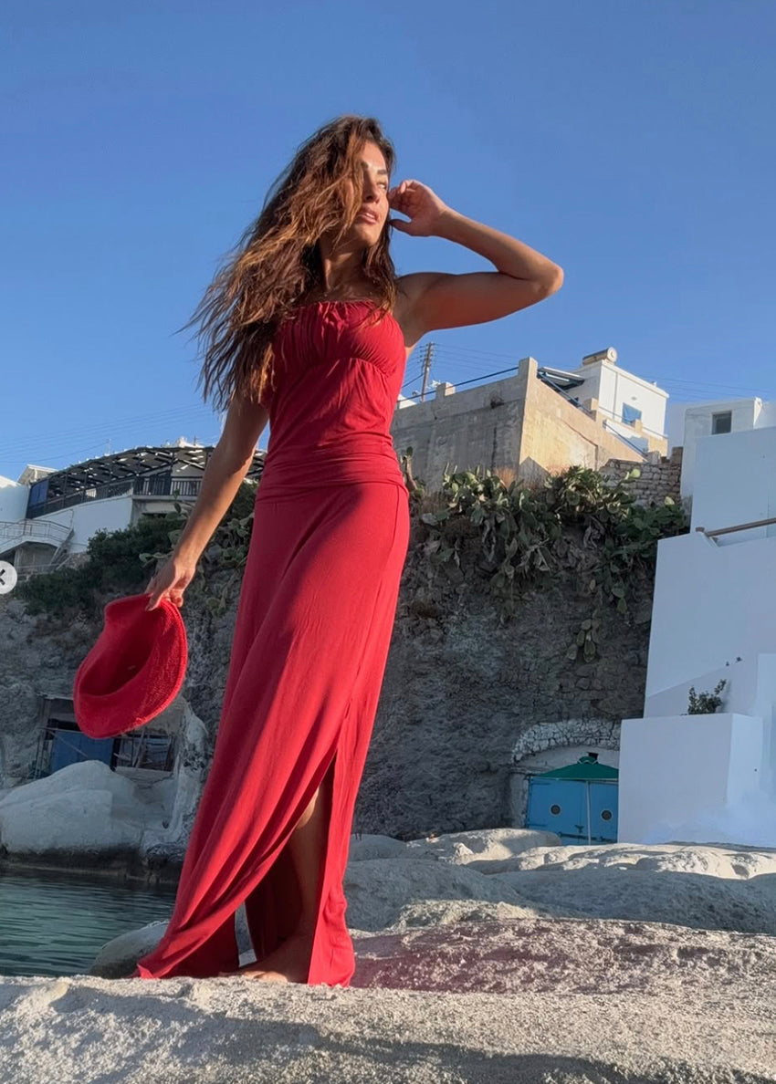Woman in a red dress standing on a scenic location with white buildings and blue sky.
