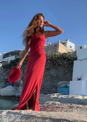 Woman in a red dress standing on a scenic location with white buildings and blue sky.