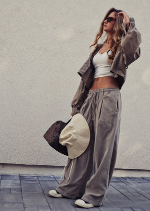 Woman in casual outfit with wide-leg pants and jacket against a plain wall.