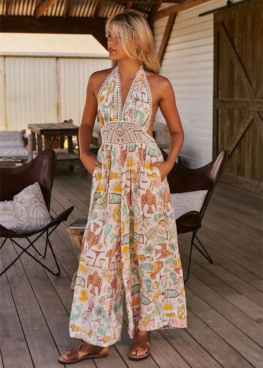 A woman standing on a porch wearing a beige and multicolor floral jumpsuit with a halter neckline and wide-leg design.