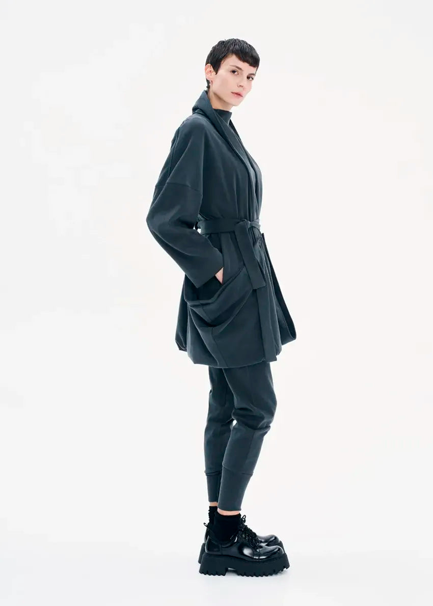 A model wearing a gray coat with a belt, featuring a buttoned front and a flowing fit.