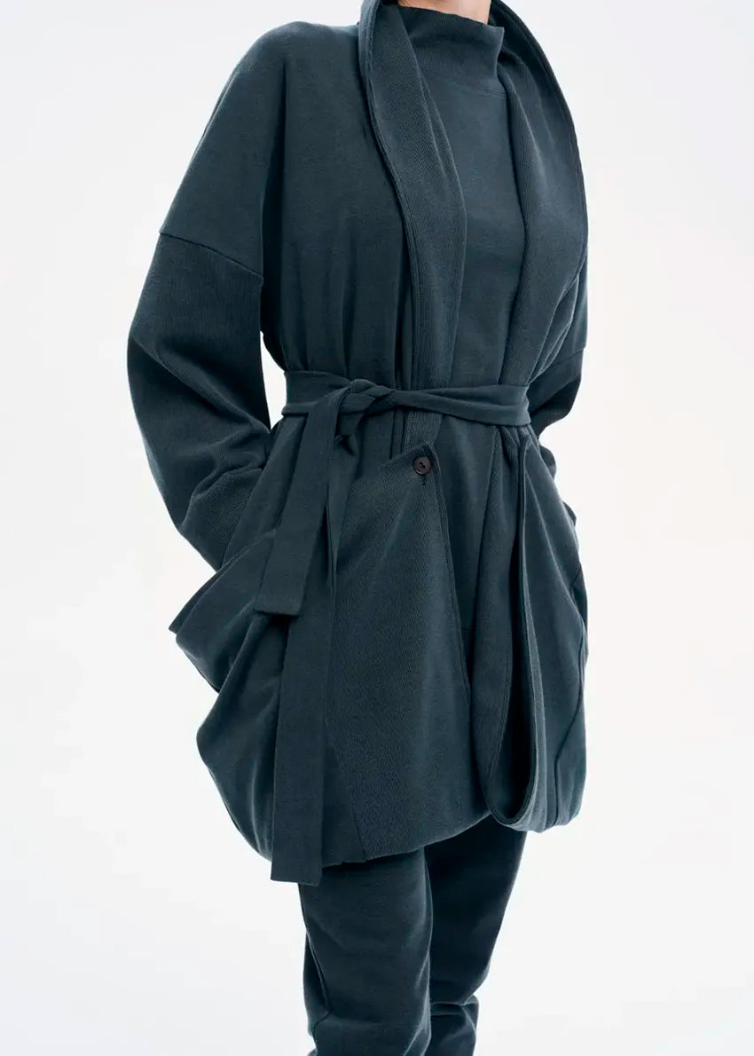 A model wearing a gray coat with a belt, featuring a buttoned front and a flowing fit.