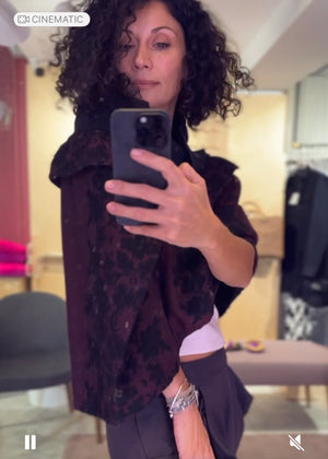 Woman taking a mirror selfie wearing a dark patterned poncho in a room with furniture.