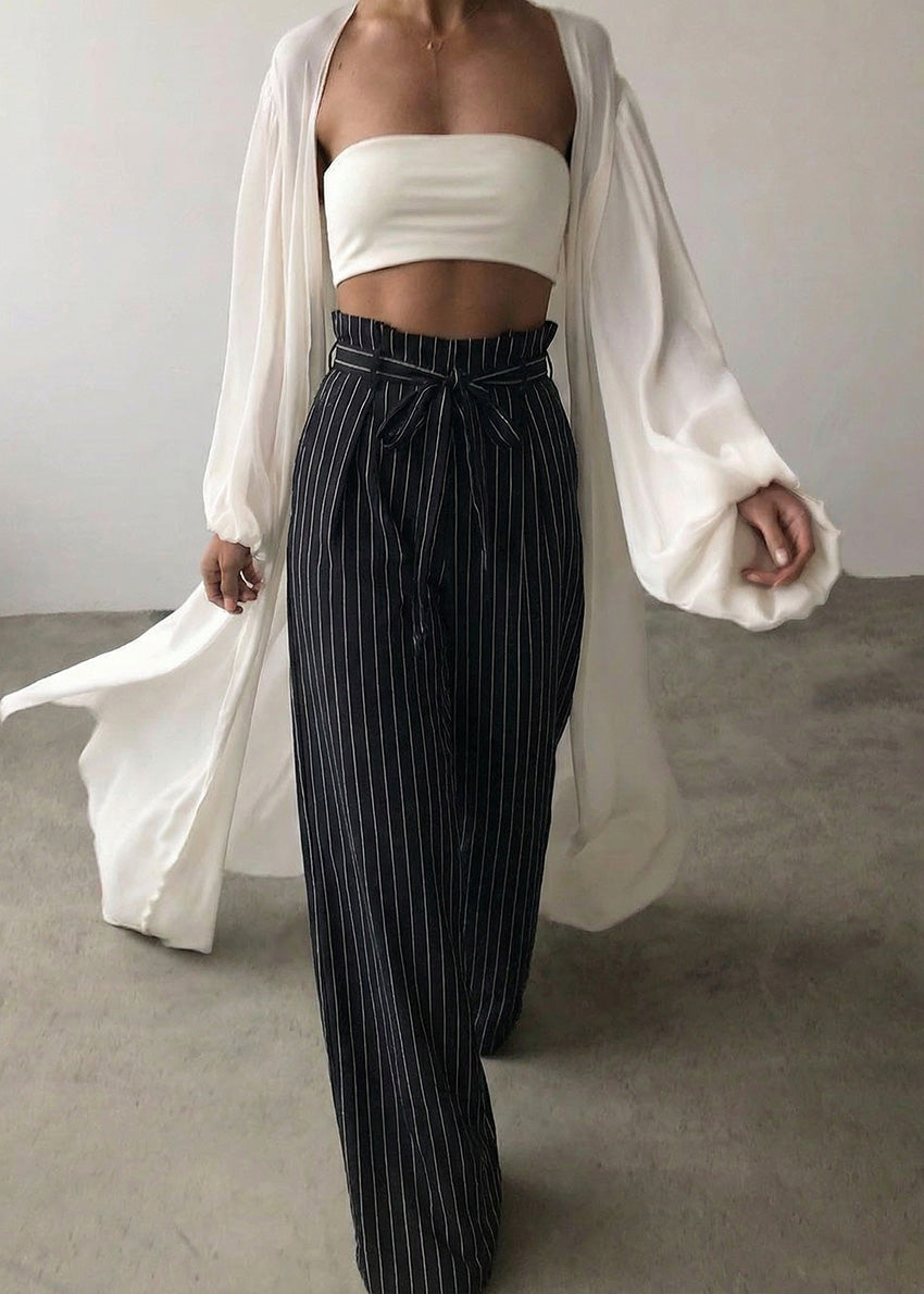 Person wearing a white strapless top and black pinstripe pants with a white cardigan.