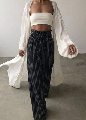 Person wearing a white strapless top and black pinstripe pants with a white cardigan.