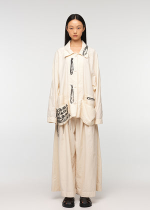 A model wearing a beige oversized jacket with an open collar, featuring four front pockets and closures with buttons. The jacket has a relaxed fit and the model is also wearing light-colored pants.