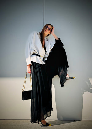 A woman wearing a white short-medium jacket with a lapel collar and black long sleeves, paired with a black wide-legged pant and sunglasses.