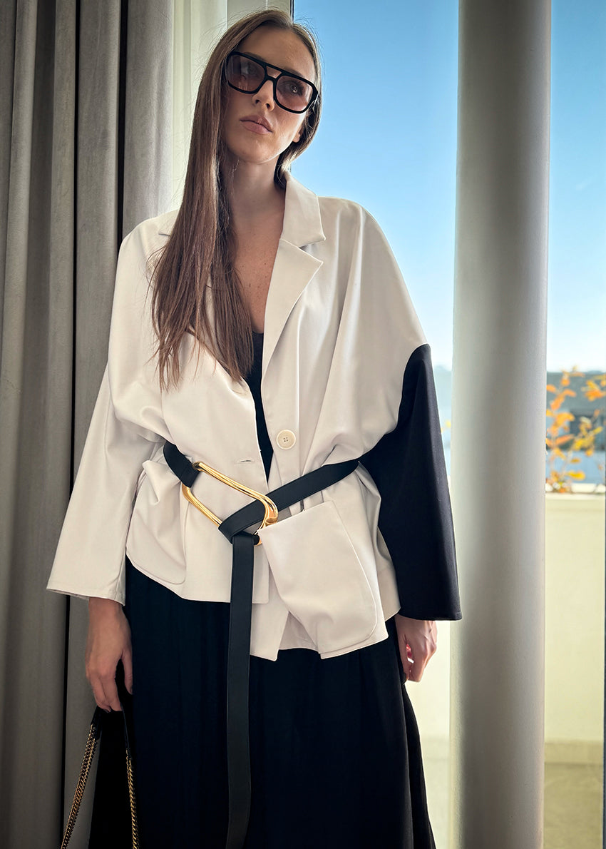 A woman wearing a white short-medium jacket with a lapel collar and black long sleeves, paired with a black wide-legged pant and sunglasses.