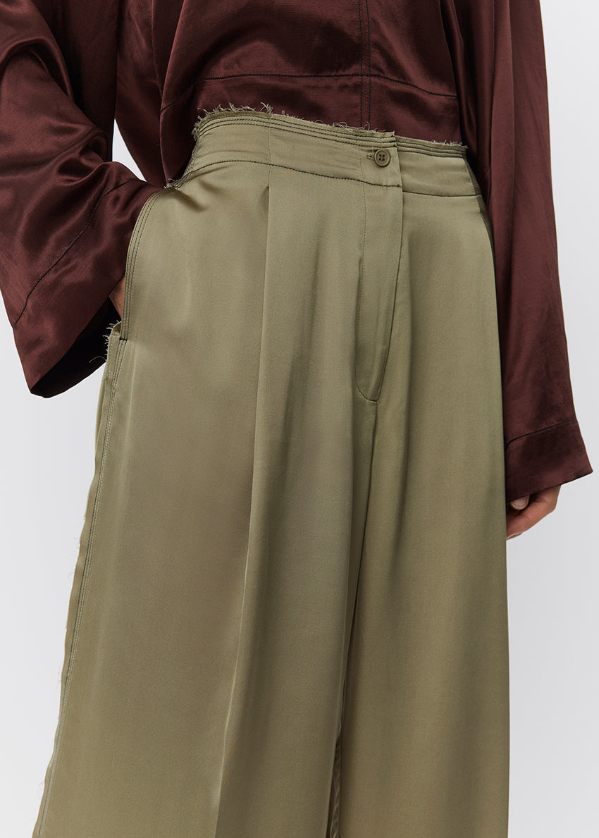 Person wearing a brown shirt and green wide-leg pants on a white background