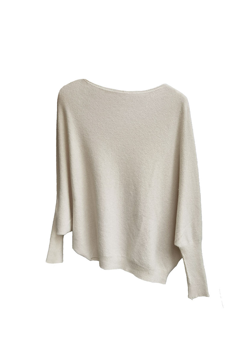 A beige, asymmetrical hemline sweater with fitted sleeves that flare out into a poncho-like shape