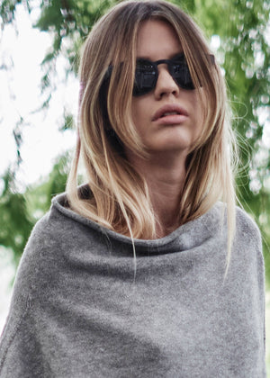 A grey, asymmetrical hemline sweater with fitted sleeves that flare out into a poncho-like shape