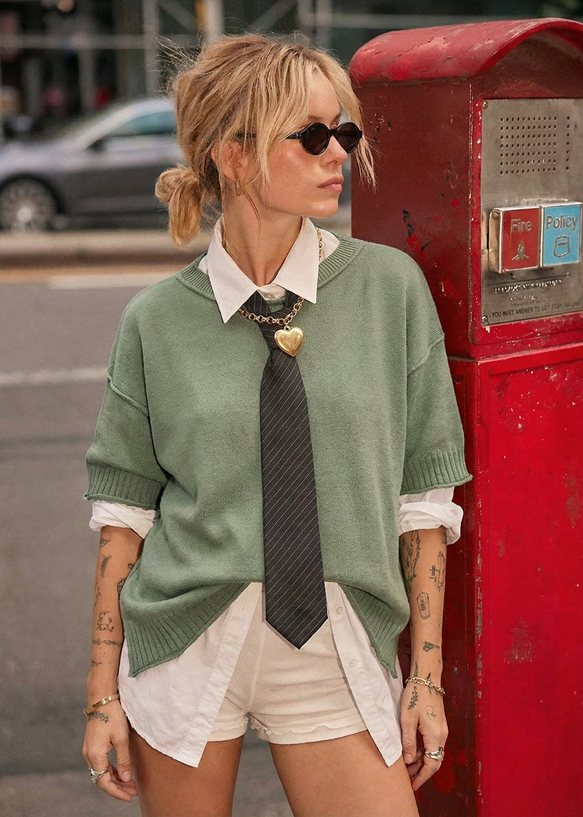 Person wearing a green sweater over a white shirt with a tie, standing next to a red postbox.