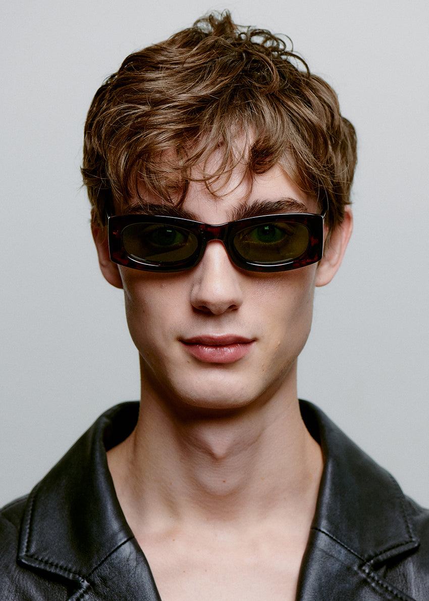 Man wearing sunglasses and a black leather jacket against a gray background