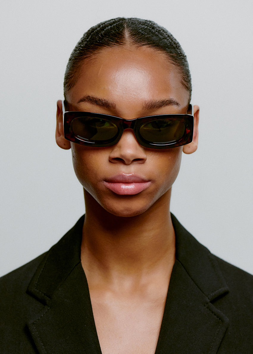 Person wearing black sunglasses and a black outfit against a plain background