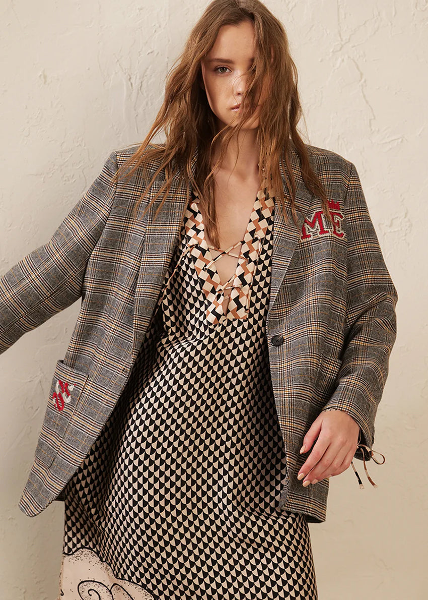 Woman wearing a plaid blazer over a patterned dress with visible branding.