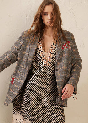 Woman wearing a plaid blazer over a patterned dress with visible branding.