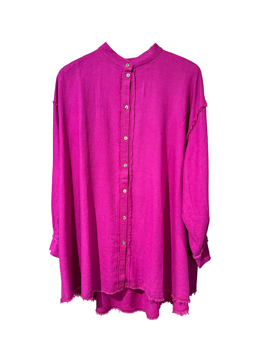 A model wearing a magenta oversized linen and bamboo blend shirt with fringes at the seams, paired with matching pants.