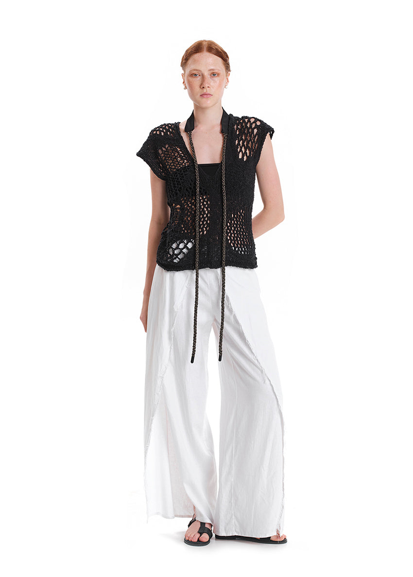 A model wearing a fringed linen top in pink and matching pants, with a yellow head accessory and white sandals.