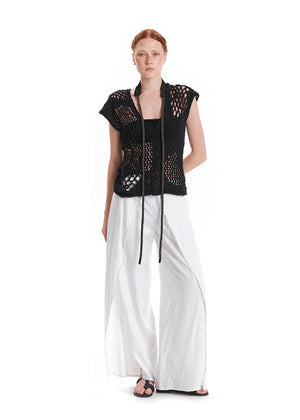 A model wearing a fringed linen top in pink and matching pants, with a yellow head accessory and white sandals.