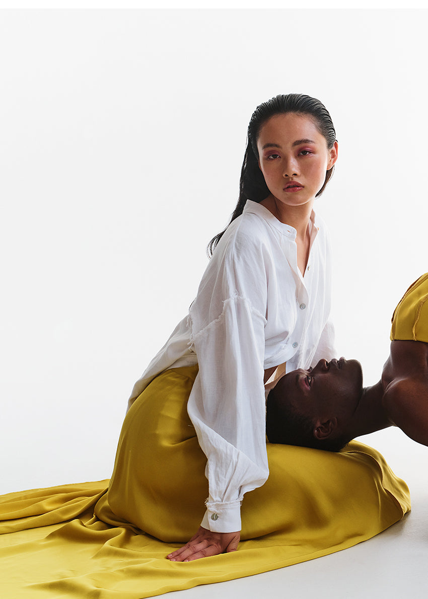 Two people sitting on a white background with one person wearing a white shirt and yellow skirt.
