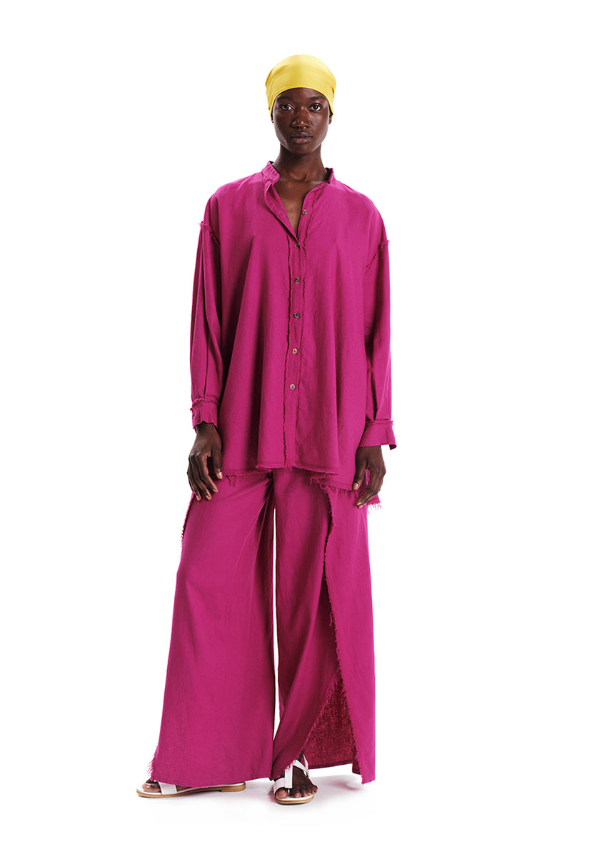 A model wearing a magenta oversized linen and bamboo blend shirt with fringes at the seams, paired with matching pants.