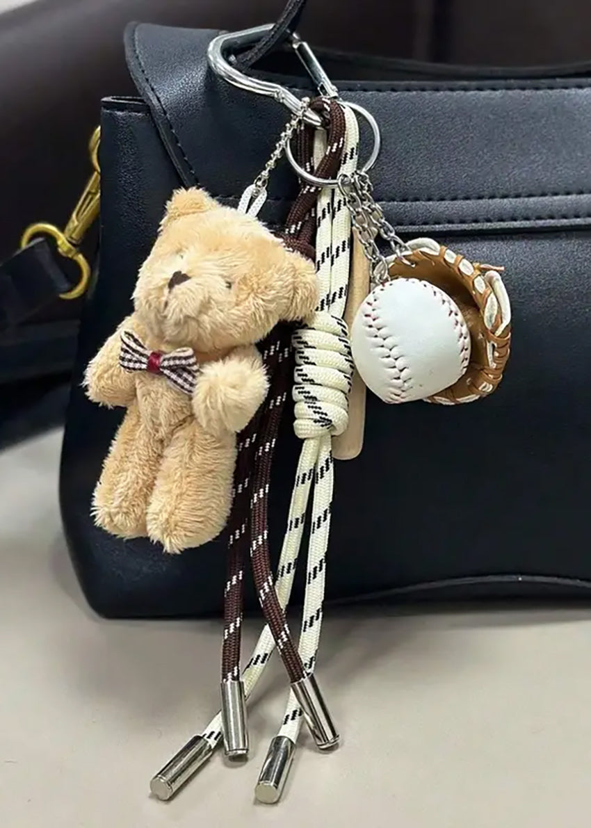 A colorful braided rope keychain with a cute bear bag pendant, a string, and baseball ornament attached to a handbag.