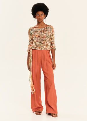 Woman wearing a patterned top and rust-colored pants on a white background