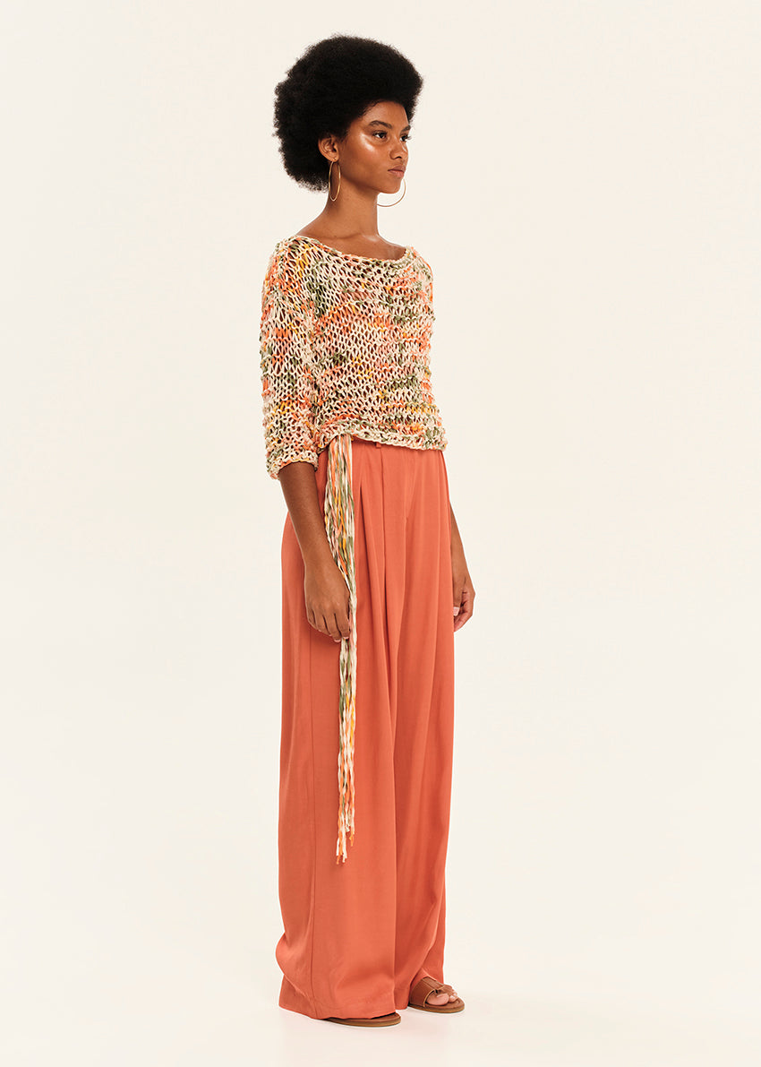 Woman wearing a patterned top and rust-colored pants on a white background