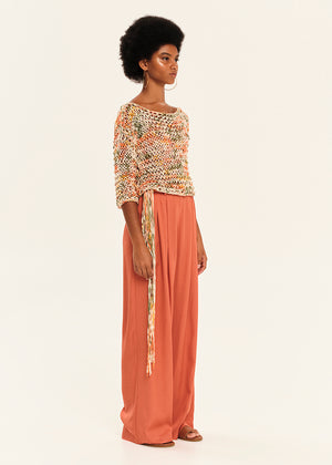 Woman wearing a colorful knit top and long pink pants on a white background