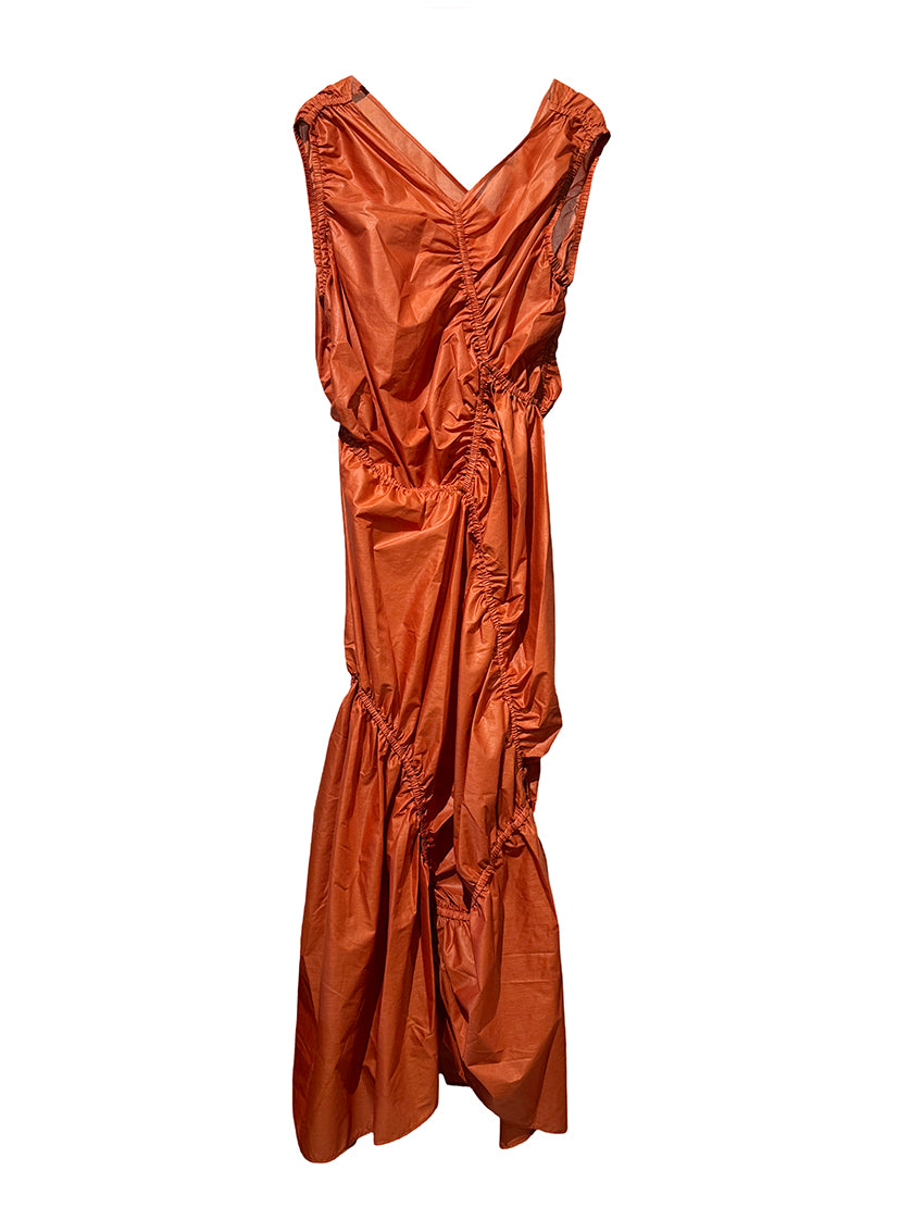 A long sleeveless asymmetrical red dress with a deep V neckline, featuring diagonal seams and gathering on all sides, modeled by a woman standing against a white background.