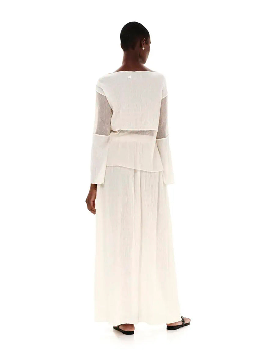 A model wearing a white high-waisted maxi skirt with textured cotton and side cut-outs, paired with a white top.