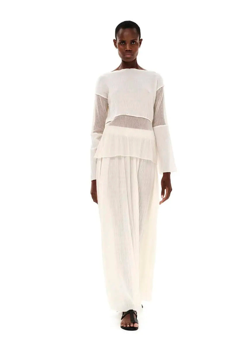 A model wearing a maxi high waisted white skirt with side cut-outs, paired with a matching top.