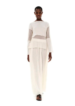 A model wearing a maxi high waisted white skirt with side cut-outs, paired with a matching top.