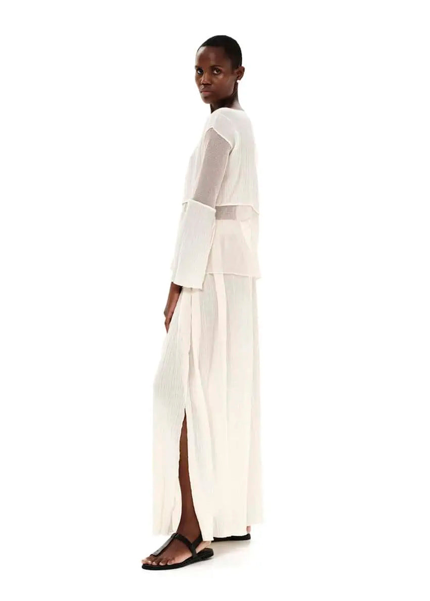 A model wearing a white high-waisted maxi skirt with textured cotton and side cut-outs, paired with a white top.