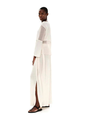 A model wearing a white high-waisted maxi skirt with textured cotton and side cut-outs, paired with a white top.