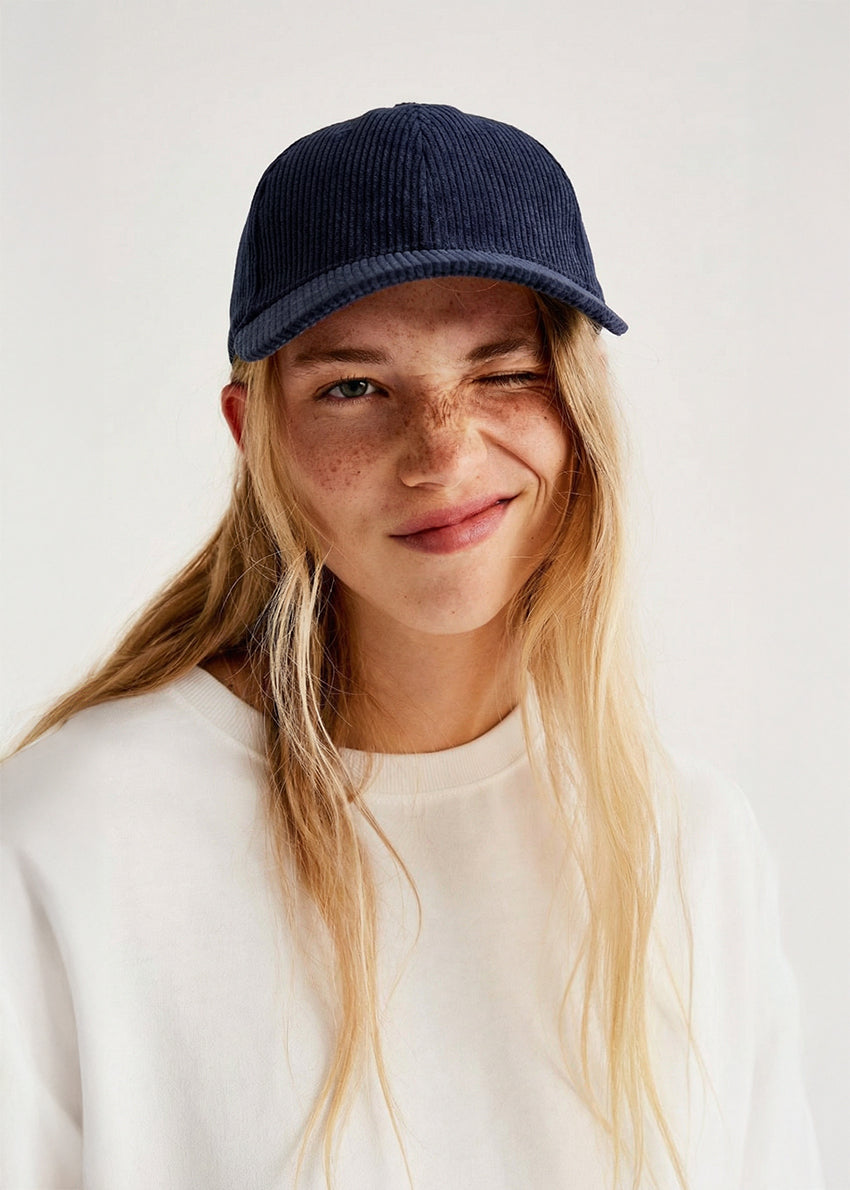 Person wearing a navy blue cap and white sweater on a light background