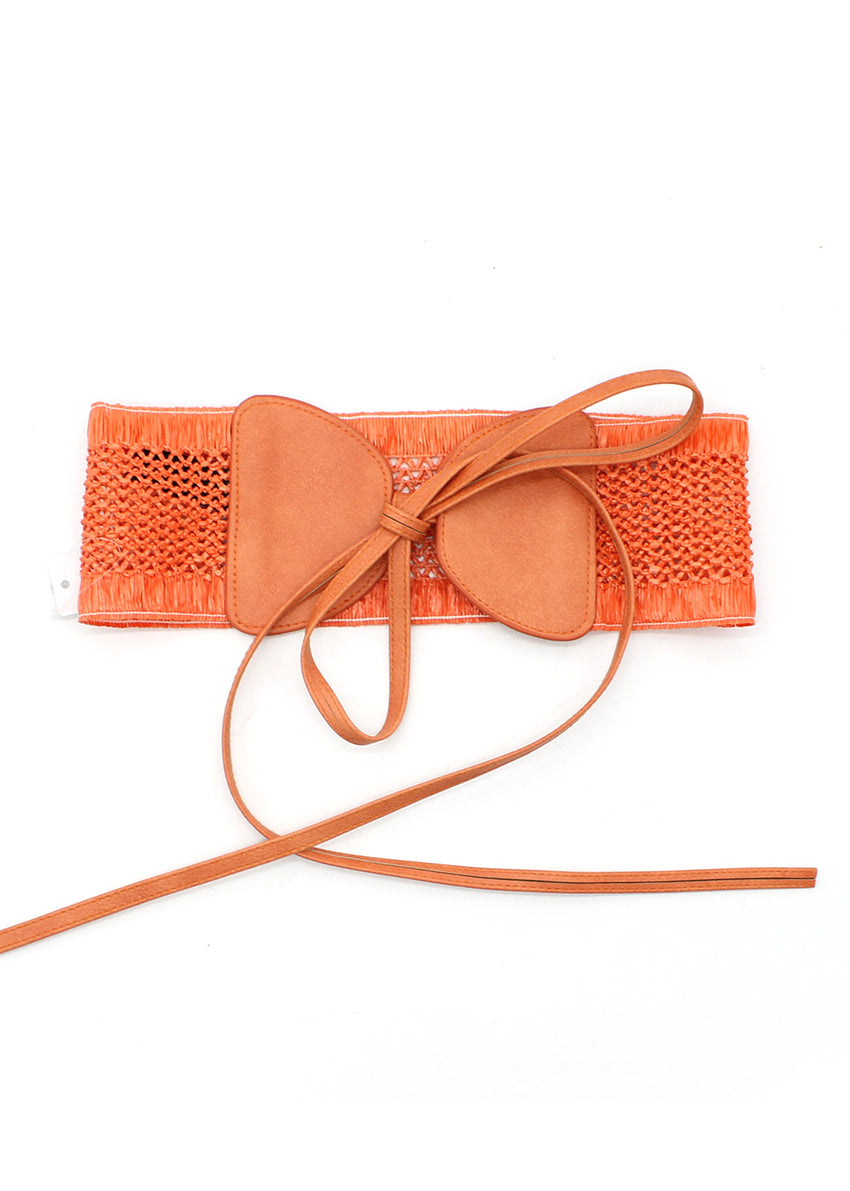A handcrafted woven waist belt with a bow accent, featuring a soft orange tone and an adjustable tie closure.