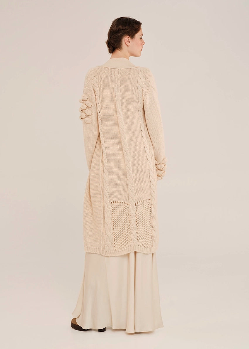 Woman wearing a beige long cardigan with a textured pattern on a plain background