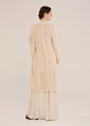 Woman wearing a beige long cardigan with a textured pattern on a plain background
