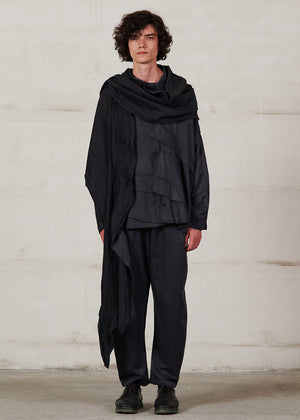 Person wearing a black outfit with a scarf against a plain background