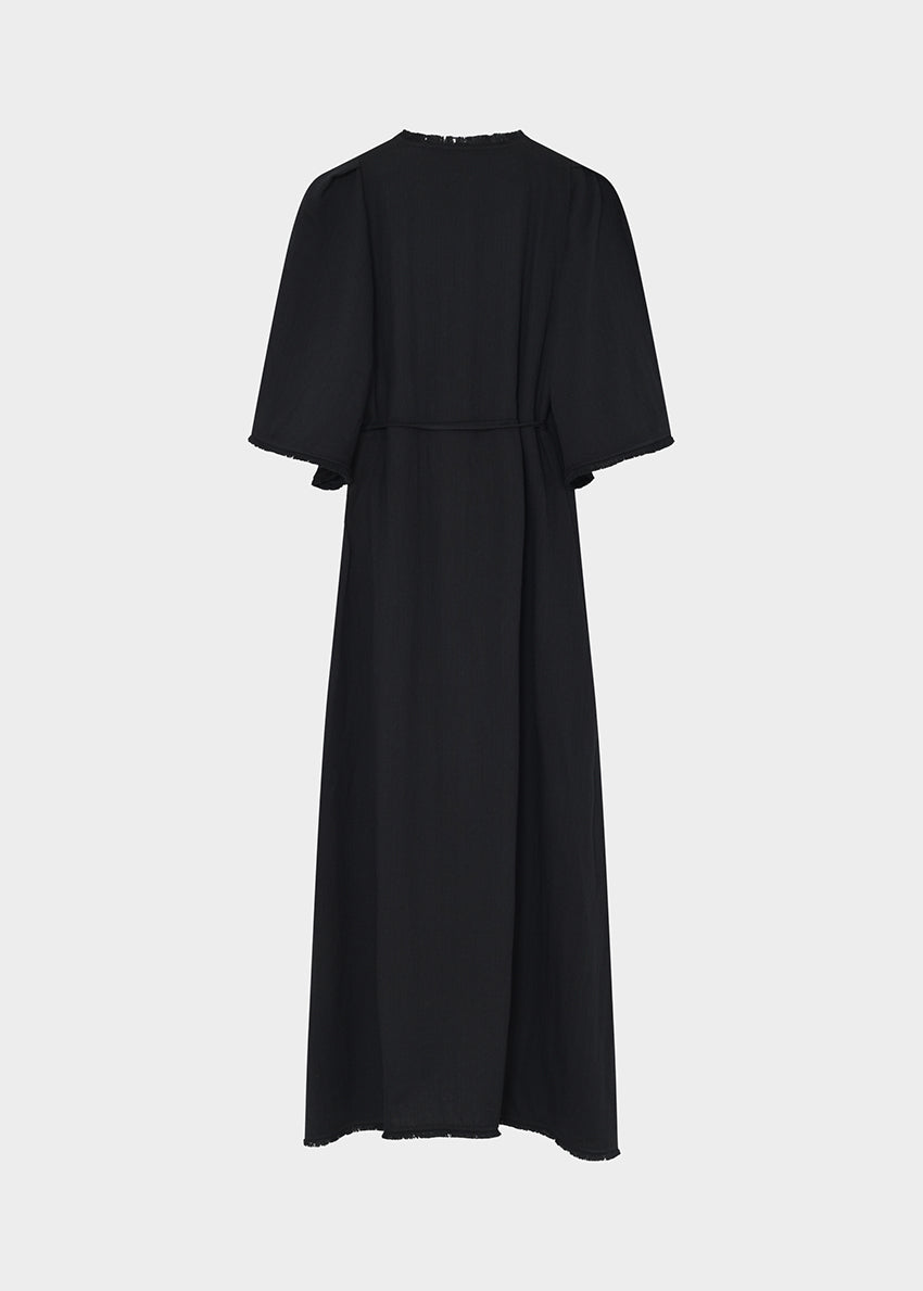 Woman wearing a black dress with cape sleeves against a neutral background