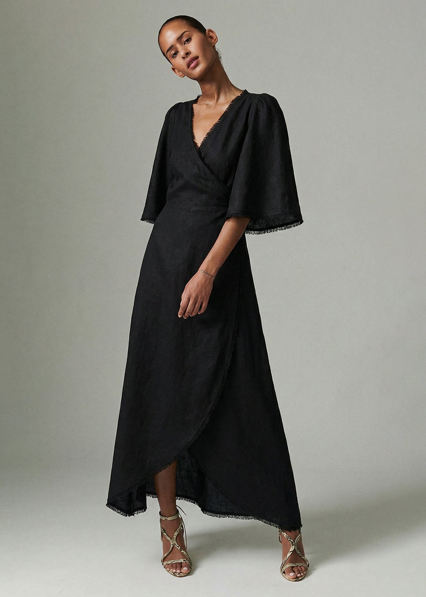 Woman wearing a black dress with cape sleeves against a neutral background