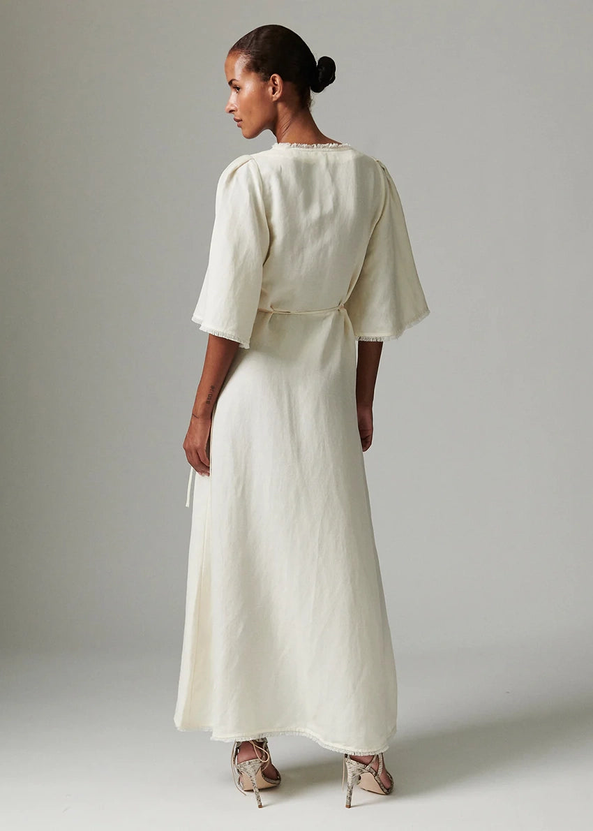 Woman wearing a long, light-colored dress against a plain background
