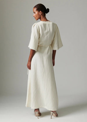 Woman wearing a long, light-colored dress against a plain background
