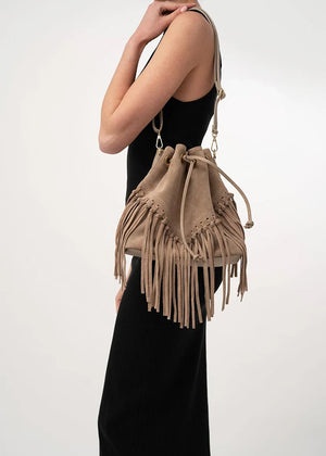 A woman wearing a black dress is seen from the back, carrying a beige suede shoulder bag with a fringe design.