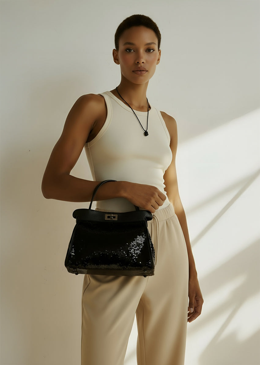 Woman holding a black handbag against a neutral background
