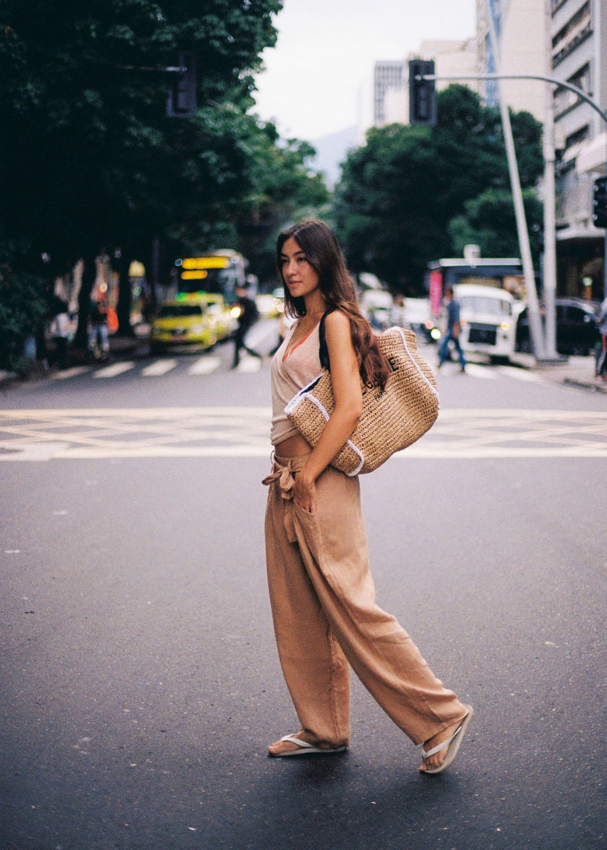 Woman walking on a city street wearing a beige outfit and carrying a woven bag.