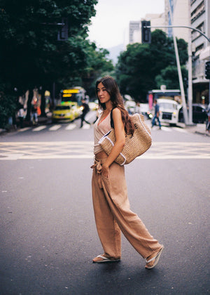 Woman walking on a city street wearing a beige outfit and carrying a woven bag.