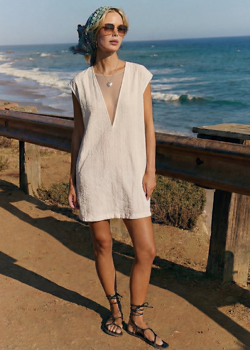 Woman in a beige dress standing on a coastal road with ocean waves in the background