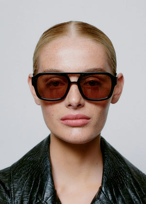 Person wearing dark sunglasses and a black leather jacket against a plain background